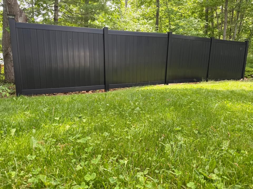 Black vinyl privacy fence installed at the edge of a wooded yard