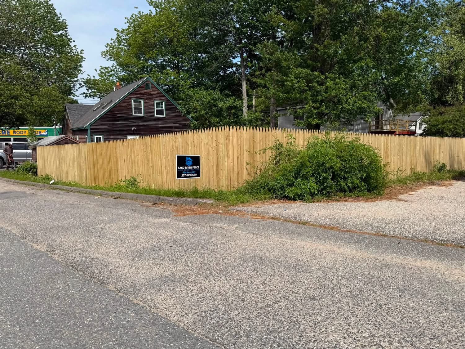 New wood stockade fence along a roadside with a Saco River Fence and Construction sign